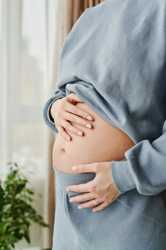 Close-up of a woman's midsection, her arms gently wrapped around her sensitive stomach.